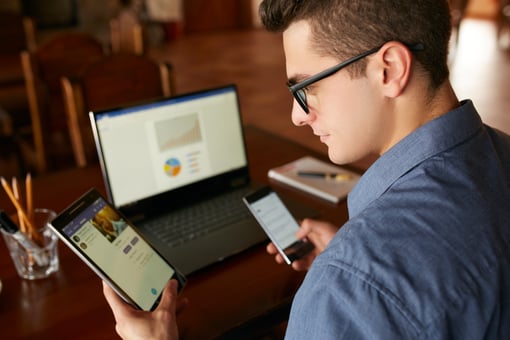 Person wearing glasses looking at multiple electronic devices.